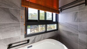 Een moderne badkamer met een badkuip, een raam met zonwering en een handdoekrek.