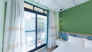 Een slaapkamer met een bed, nachtkastje, groene muur en een raam met gordijnen.