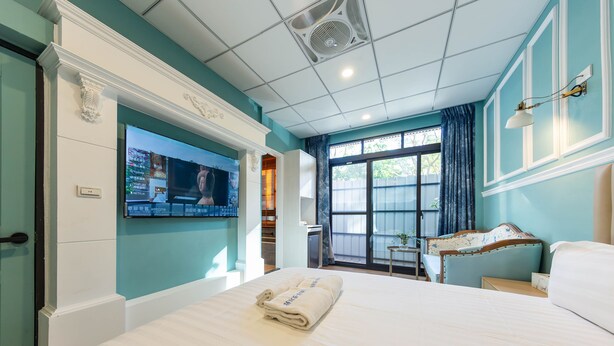 Een hotelkamer met een groot bed, een aan de muur bevestigde televisie en een raam met gordijnen.