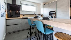 Una cocina moderna con una isla central, dos taburetes azules para bar y un horno empotrado.