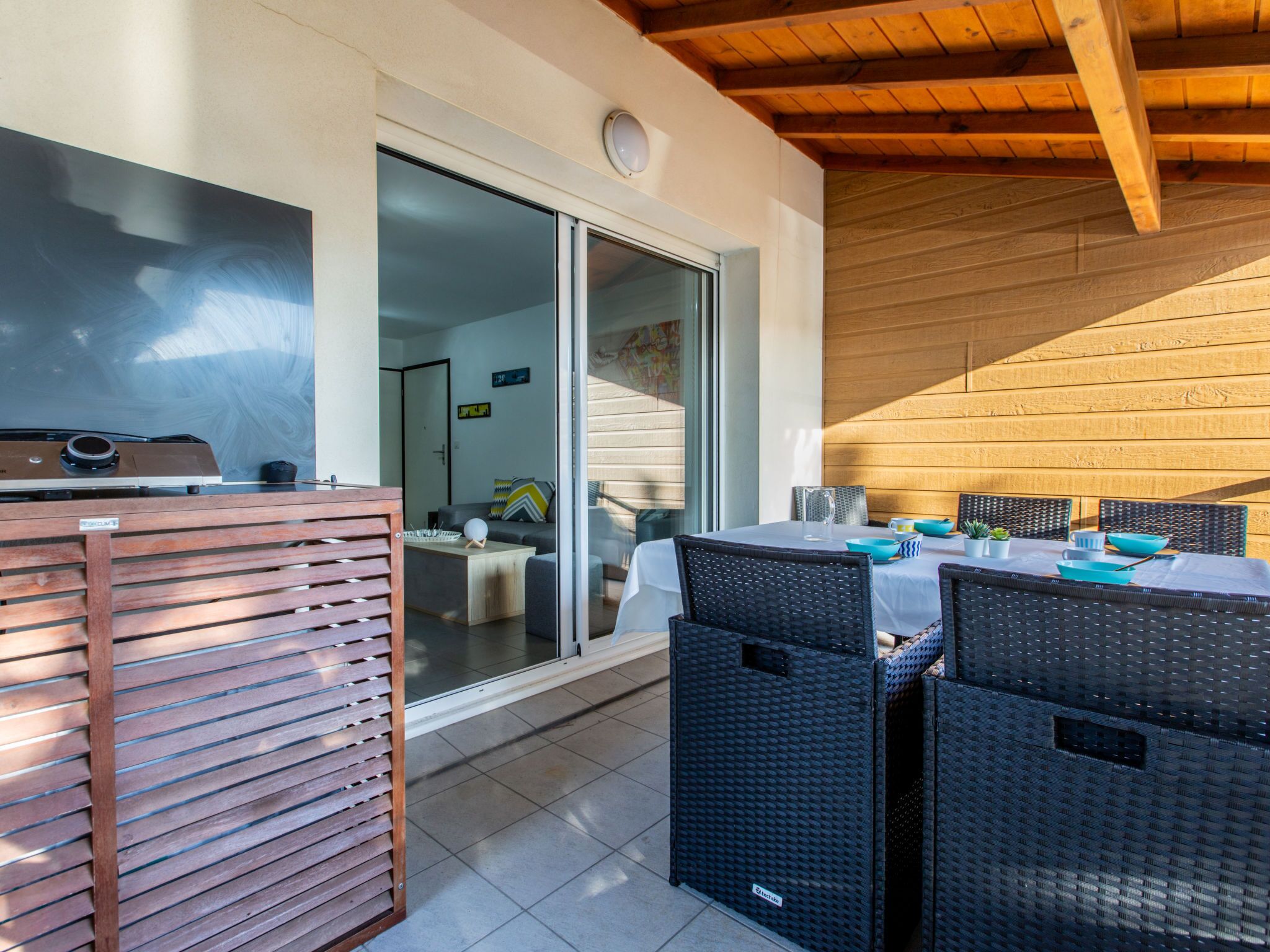 Un área de comedor al aire libre con una mesa y sillas, un ventanal corredero que da a un espacio interior y un techo de madera.
