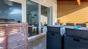 Un área de comedor al aire libre con una mesa y sillas, un ventanal corredero que da a un espacio interior y un techo de madera.