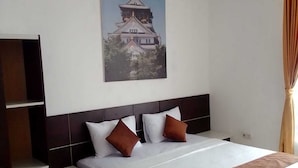 A hotel room with a bed, a headboard, a wall-mounted air conditioner, and a painting of a castle.