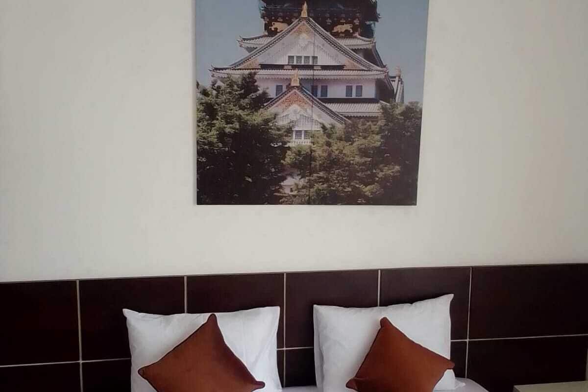Une chambre d’hôtel avec un lit, deux oreillers et un grand tableau représentant un bâtiment traditionnel japonais accroché au mur.