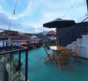 Ein Balkon mit Tisch und Stühlen, einem grünen Sonnenschirm und Blick auf die umliegenden Gebäude.
