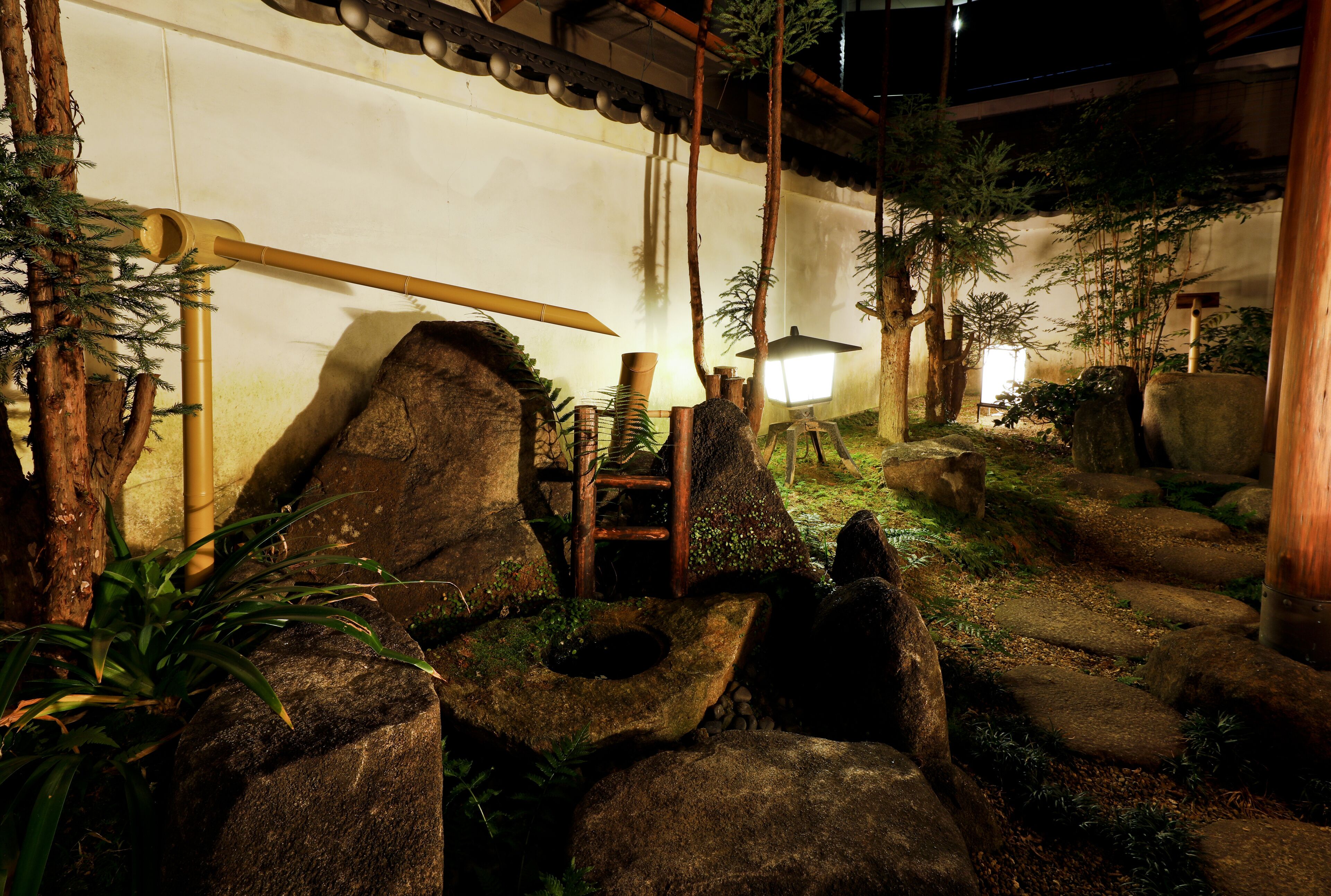Ein traditioneller japanischer Garten mit Felsformationen, Bambus und einer Holzbrücke.