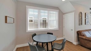 A dining area with a round table and four chairs, a large window with blinds, a door, and a brown leather couch. - Zuzu's Petals 3 bed 4 bath (Ottawa)