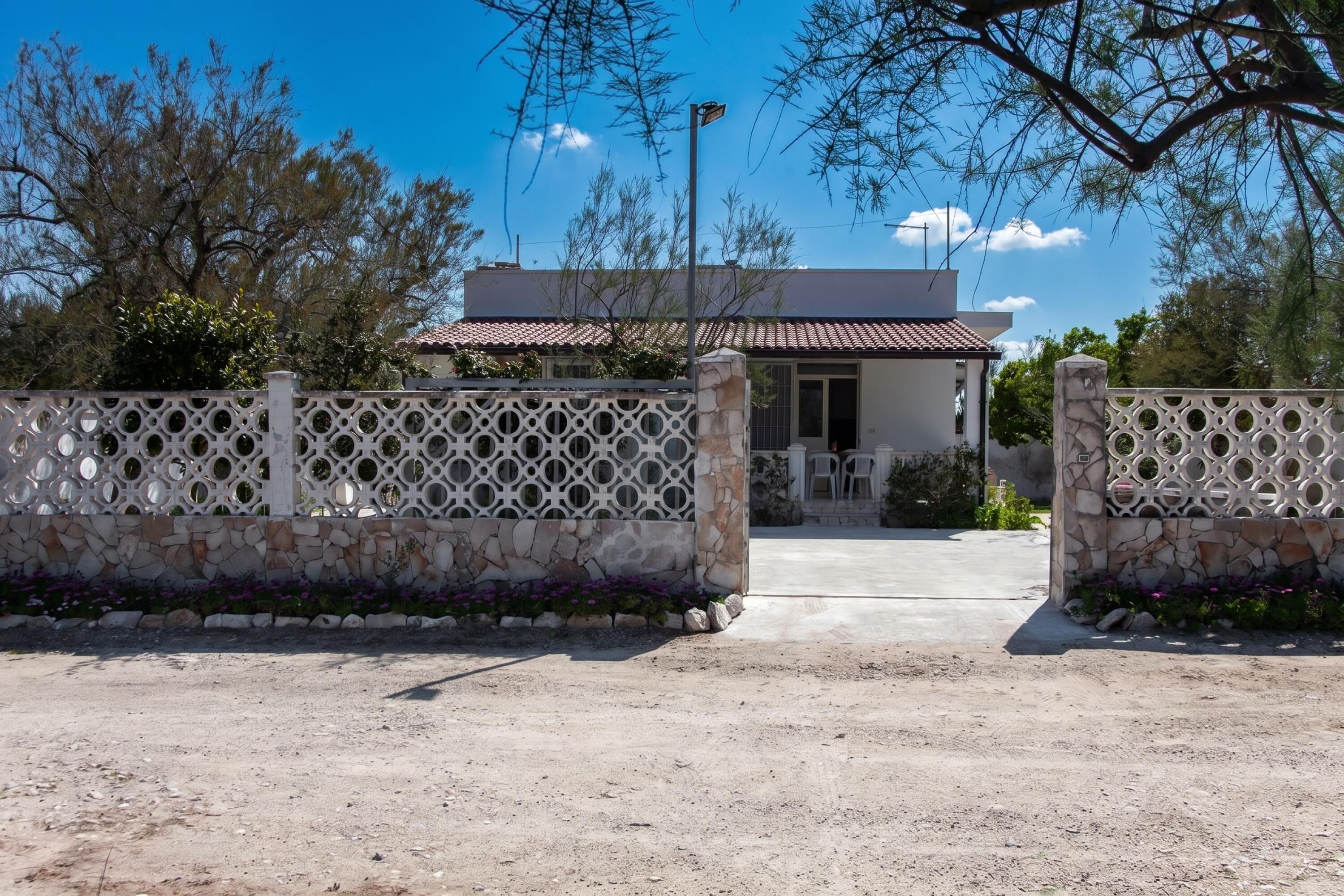 A gated entrance with a stone wall and a metal gate, leading to a building with a tiled roof and a visible door.