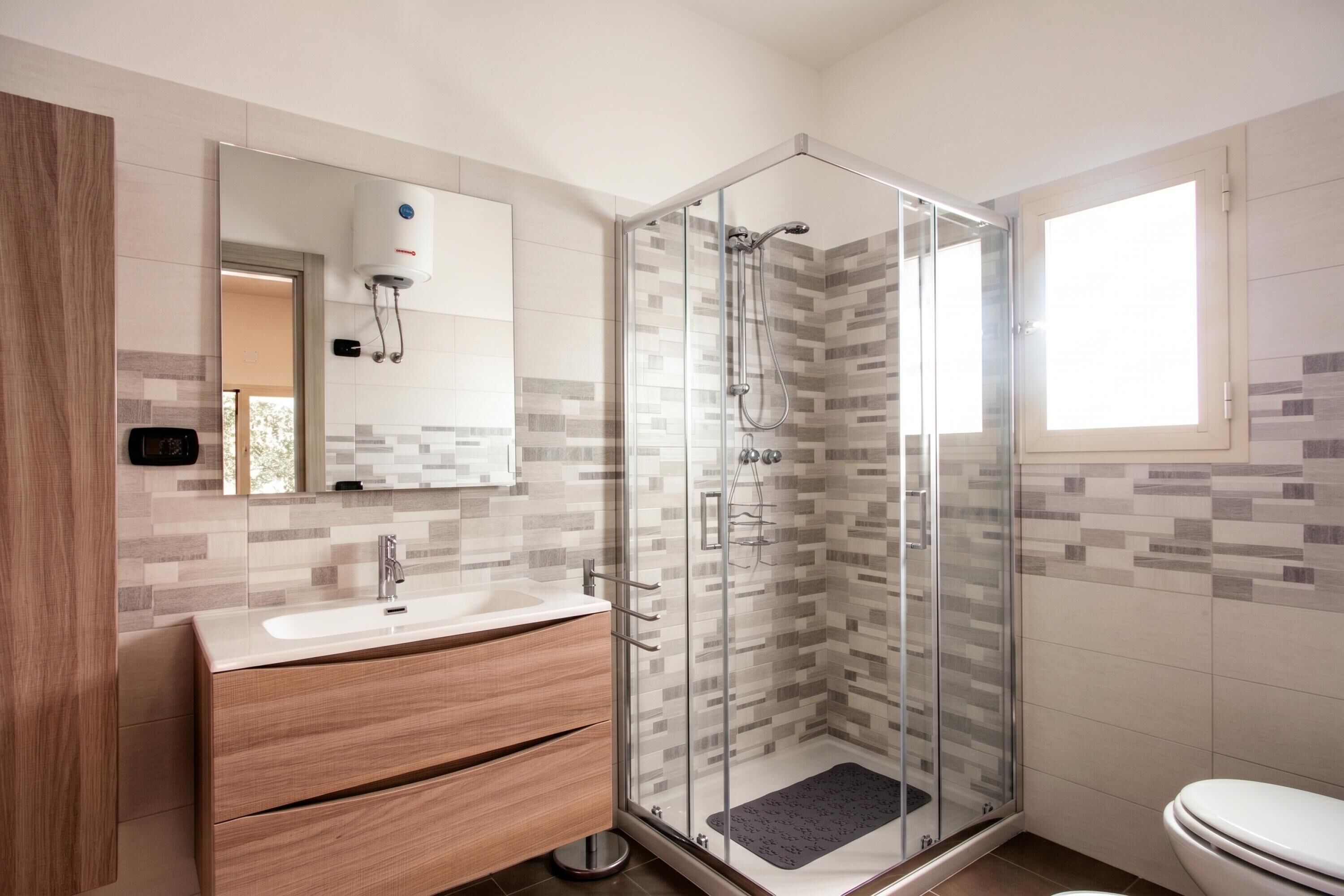 A modern bathroom with a glass-enclosed shower, a wooden vanity, and a white toilet.