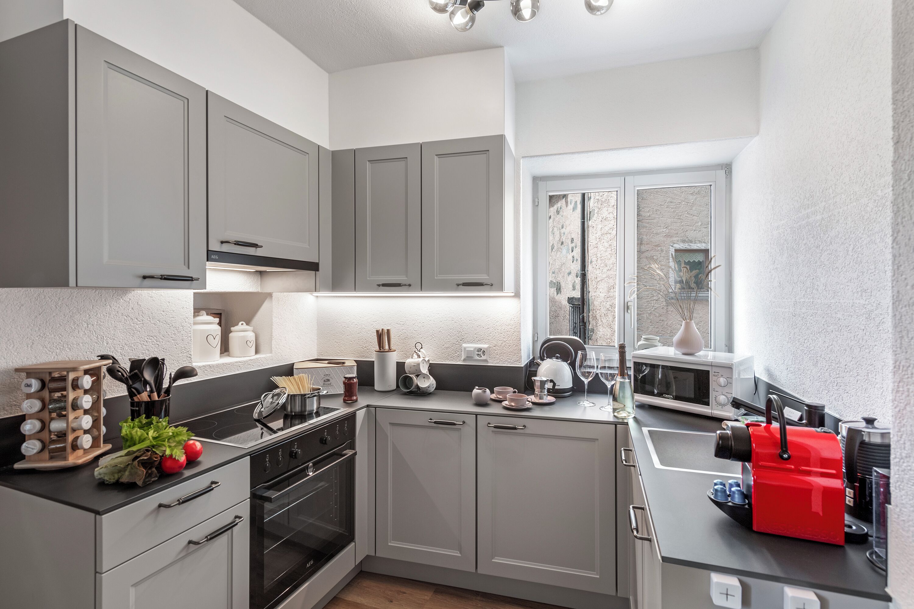 A modern kitchen with grey cabinets, a black countertop, and a red kettle.
