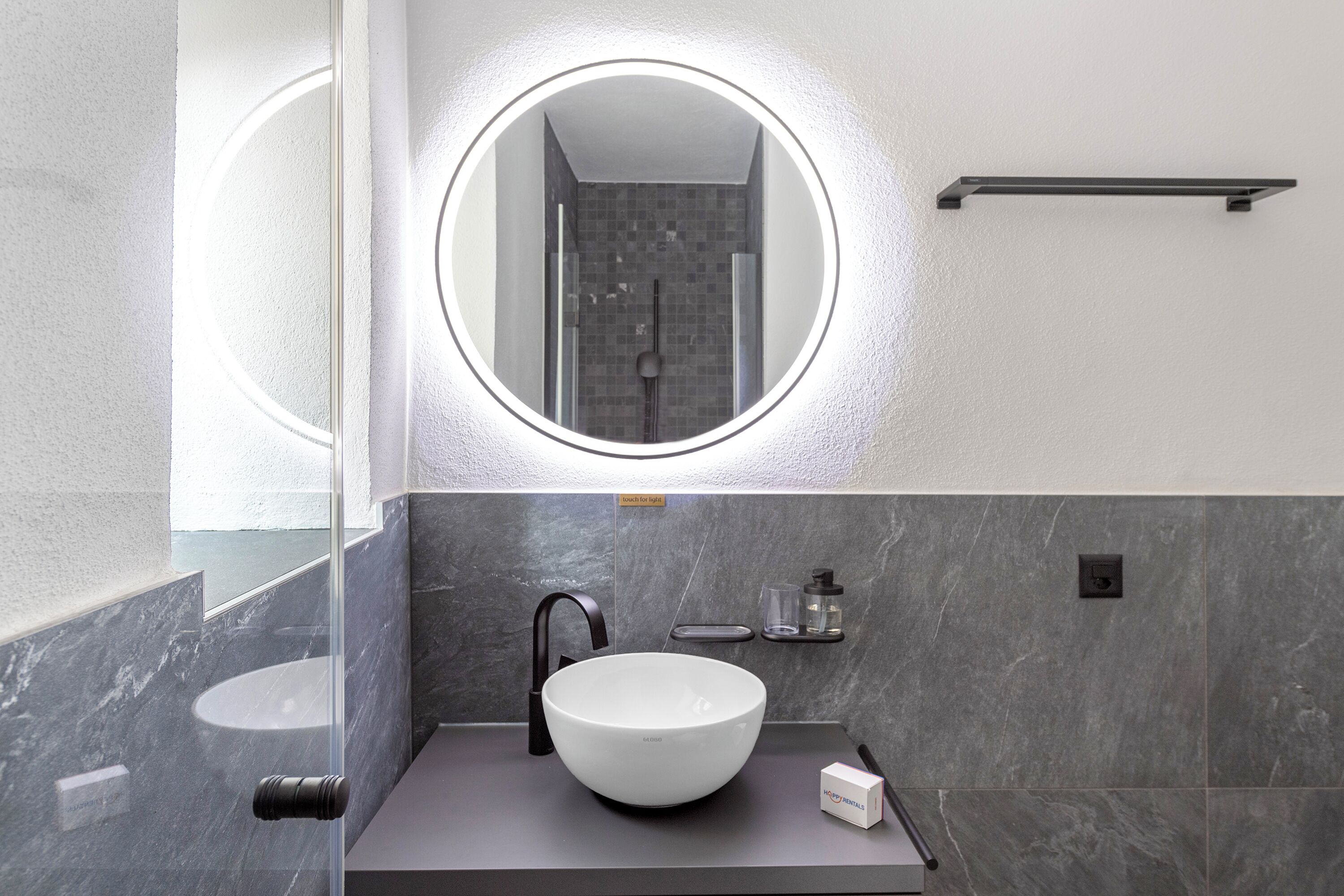 A modern bathroom with a round mirror, a white sink, and a shower area.