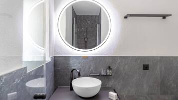 A modern bathroom with a round mirror, a white sink, and a shower area.