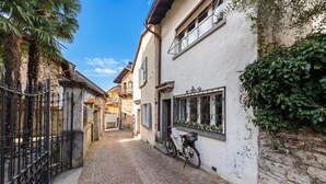 A narrow cobblestone street with buildings on either side, a bicycle parked against a wall, and a metal gate. - Casa Oliva - Boutique Townhouse in Ascona (Ascona)