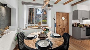A dining area with a wooden table set for four, surrounded by black chairs. A window with a view of the outside is visible, and a kitchen area is to the right. - Casa Oliva - Boutique Townhouse in Ascona (Ascona)