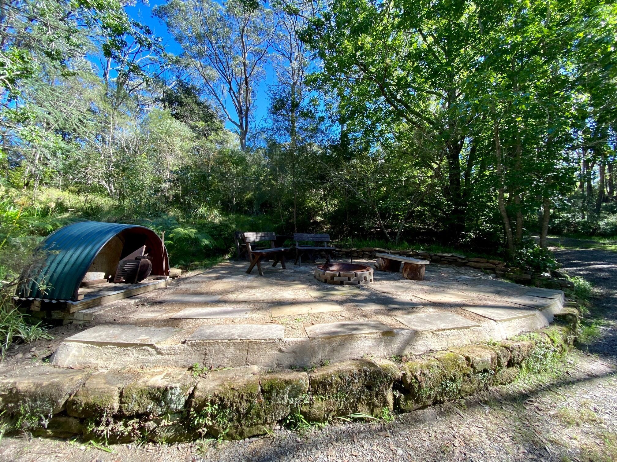 A rustic outdoor setting with a covered area, stone seating, and a bench.