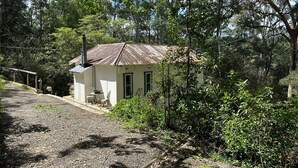 Un petit bâtiment rustique, surmonté d’un toit en métal, entouré d’une végétation luxuriante et d’arbres.