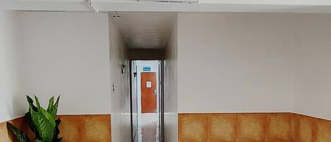 A hallway with a 'SALIDA' sign, leading to an exit door. The floor is tiled, and there is a potted plant on the left.