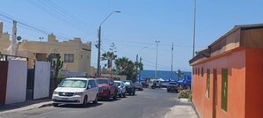 A narrow street lined with parked cars and buildings, leading to a body of water.