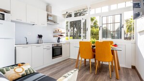Una cocina moderna con armarios blancos, horno empotrado y comedor con mesa y sillas.