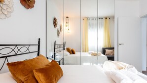 Habitación de hotel con una cama grande, dos almohadas marrones, una mesita de noche, un espejo y vistas a la ciudad por la ventana.