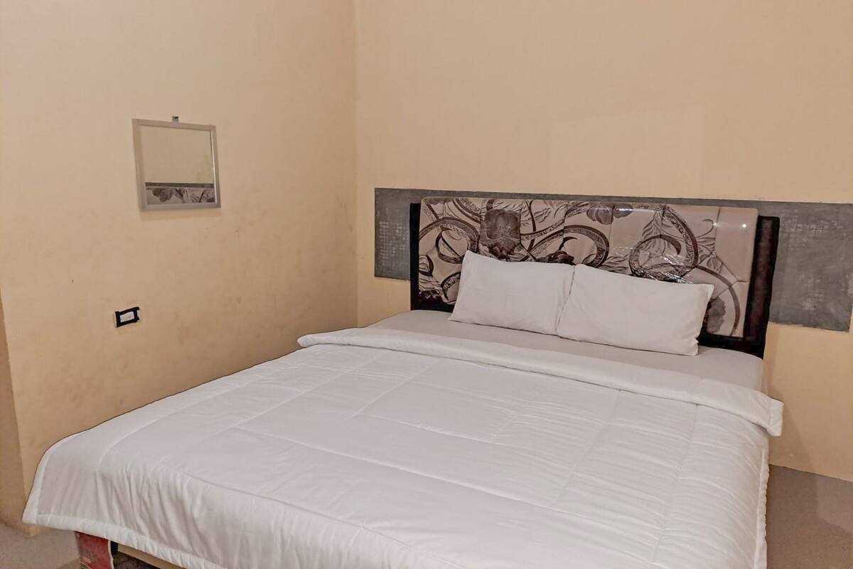 A neatly made bed with a white bedspread and two pillows, a headboard with a floral pattern, and a small wall-mounted mirror.