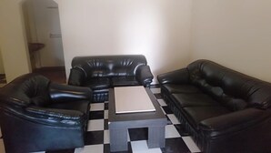 A living room with a black and white checkered floor, two black leather sofas, and a central coffee table. - OYO Life 93590 Penginapan Palapa 10 Syariah (Bandar Lampung)