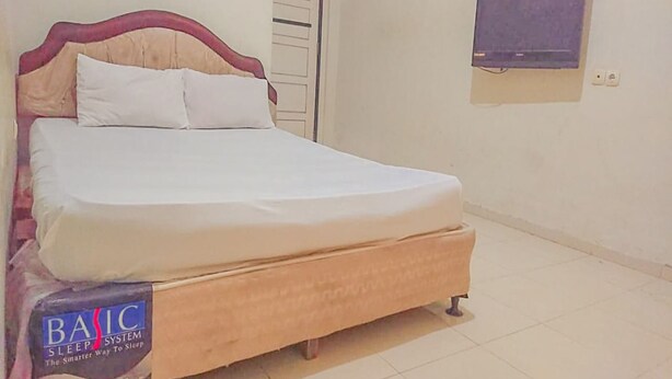 A bed with a wooden frame and white bedding, a clock on the wall, and a television mounted above it. - OYO Life 93590 Penginapan Palapa 10 Syariah (Bandar Lampung)