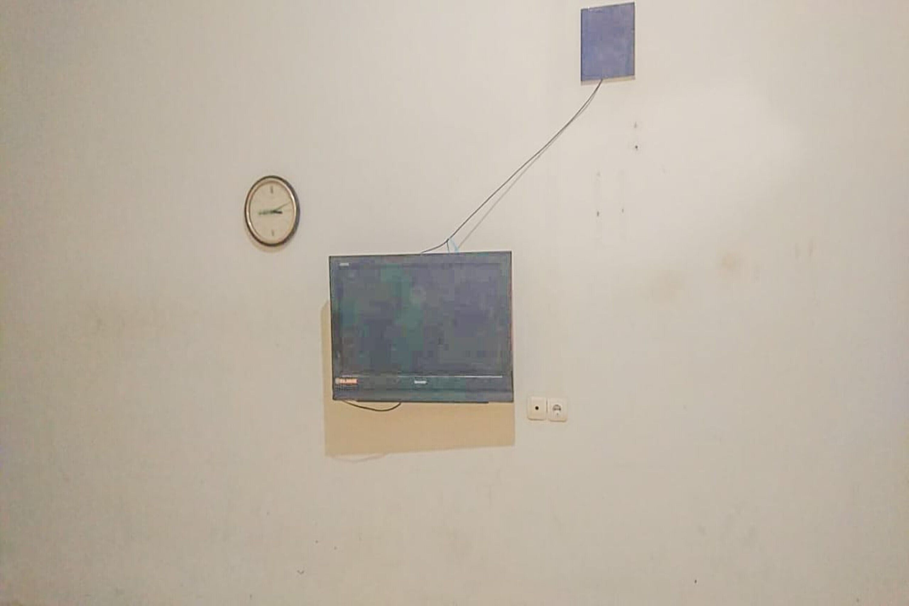 A wall-mounted television with a clock and a power outlet.