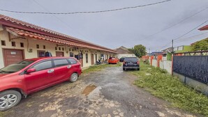 A narrow street with a red car parked on the left and a black car on the right. There are buildings on both sides of the street, with a fence on the right side. - OYO Life 93590 Penginapan Palapa 10 Syariah (Bandar Lampung)