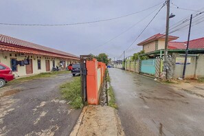 Une rue résidentielle bordée de maisons, avec une voiture rouge et une moto garées sur le côté.