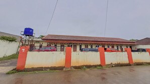 A building with a red-tiled roof, a blue water tank, and a gated entrance with parked cars. - OYO Life 93590 Penginapan Palapa 10 Syariah (Bandar Lampung)