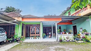 A house with a green and orange facade, a tiled roof, and a front porch with potted plants. - SPOT ON 93592 Pondok Backpackers Ardafa JogjaNearBlue Lagoon Jogja (Ngemplak)