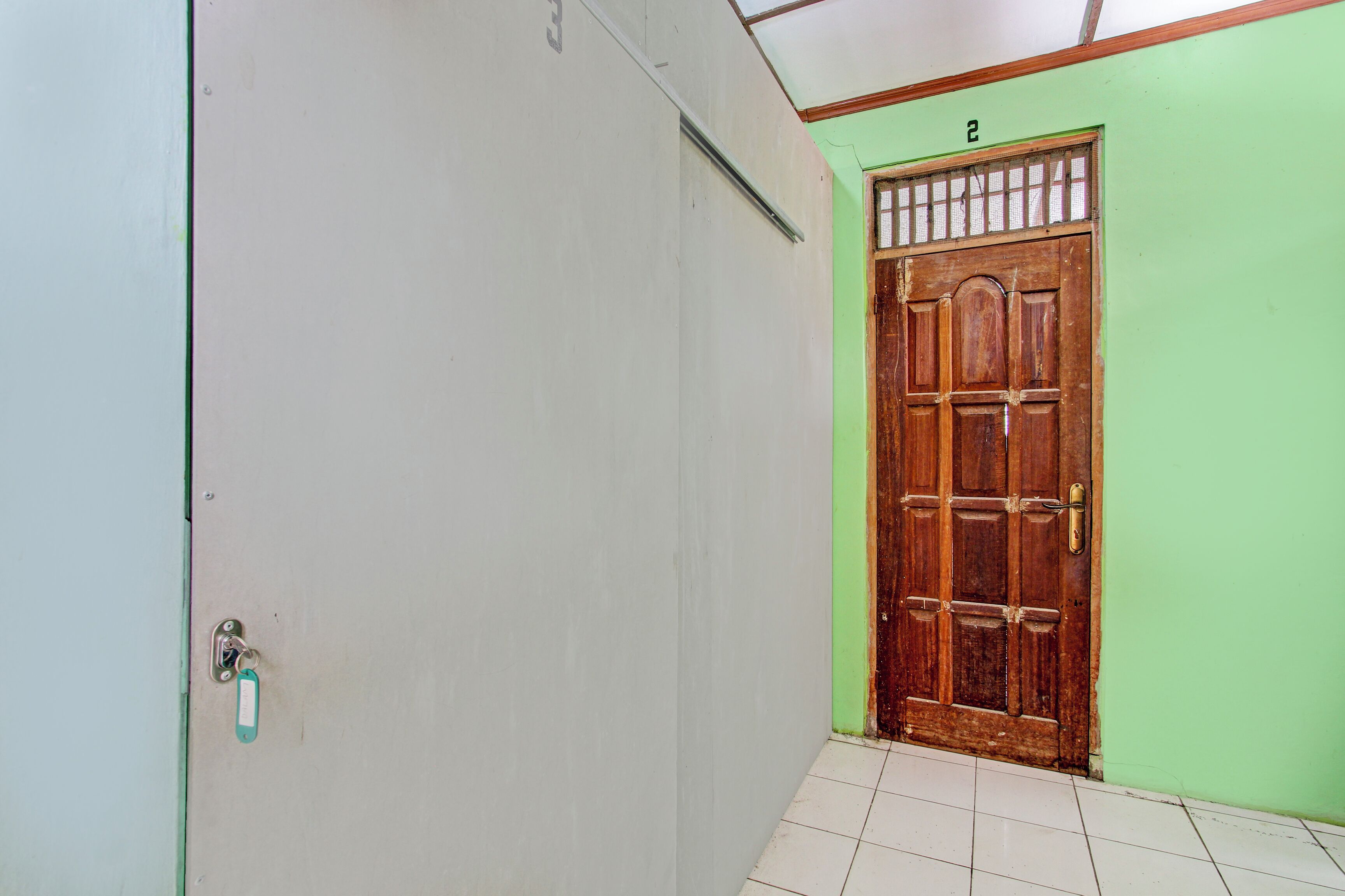 A hallway with a wooden door, a green wall, and a tiled floor.