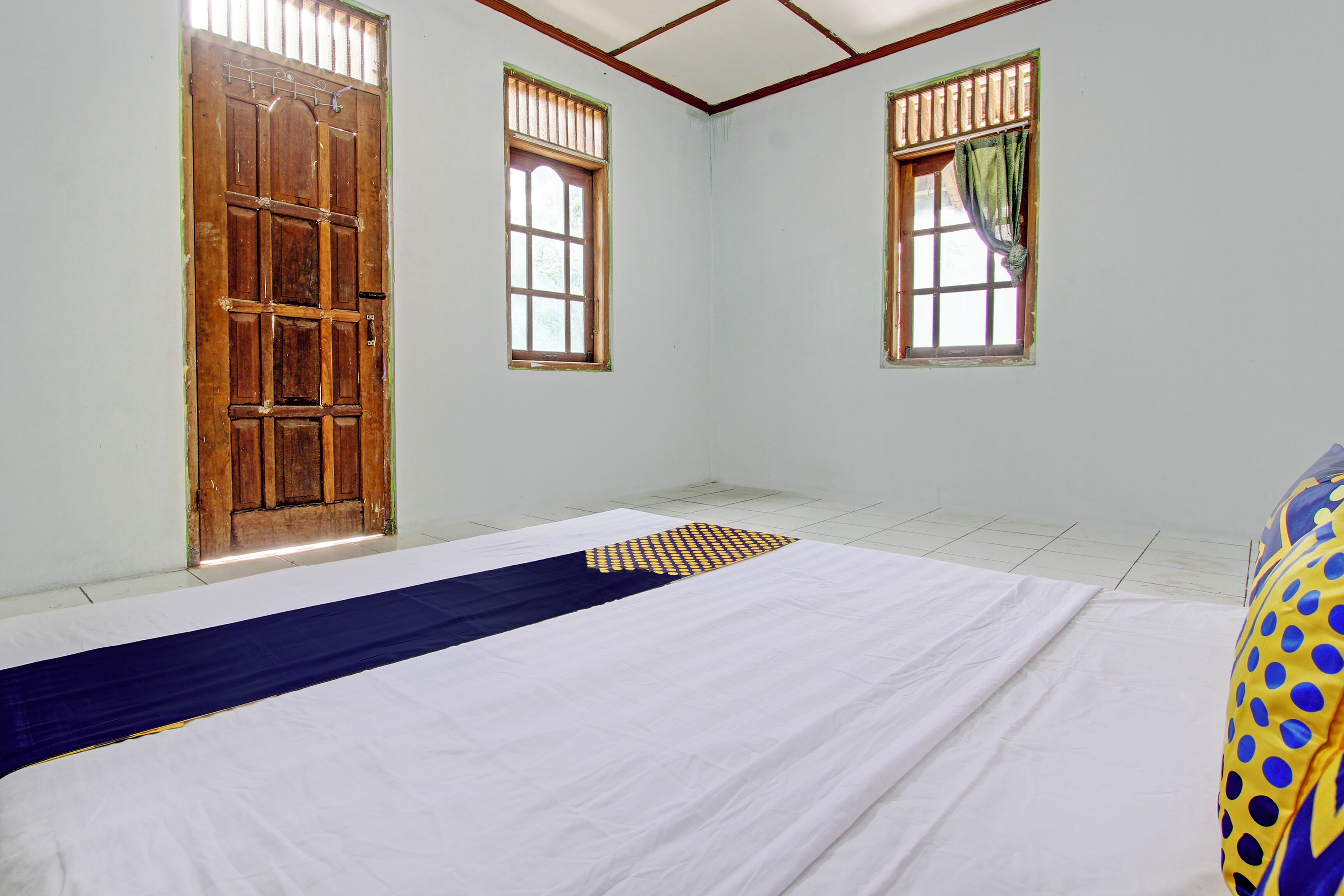 A room with a large bed, two windows, and a wooden door.