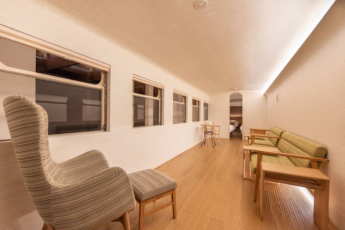 A spacious room with a high ceiling, a wooden floor, a striped armchair, a sofa, and a small table.