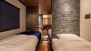 A narrow hallway with two beds, wooden ceiling, stone wall, and a window with blinds. - Kisyapoppo (Nakatsu)
