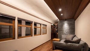 A modern interior with a wooden ceiling, a stone accent wall, a grey sofa, and a small round table. - Kisyapoppo (Nakatsu)