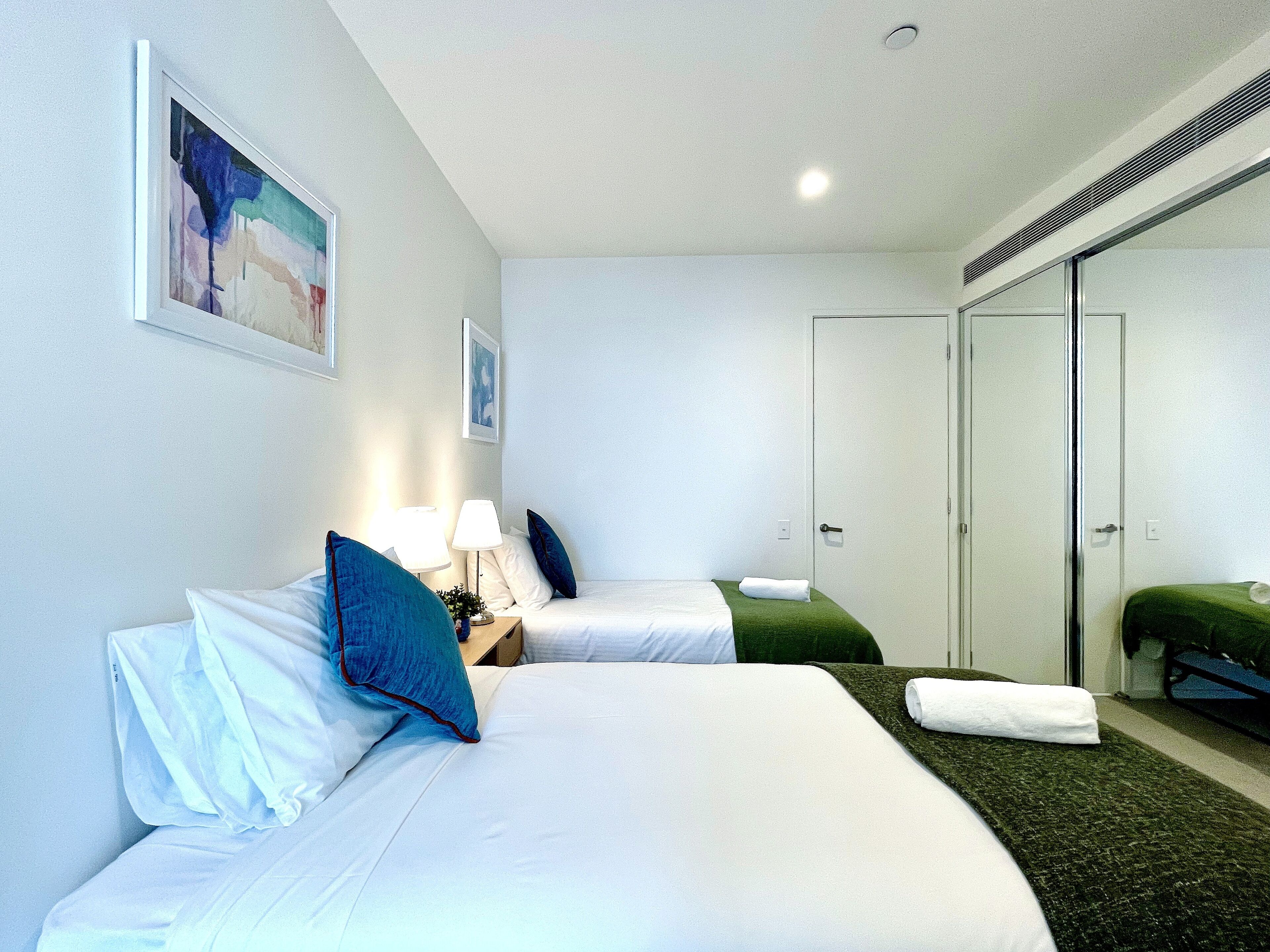 A hotel room with two beds, a mirror, and a door.