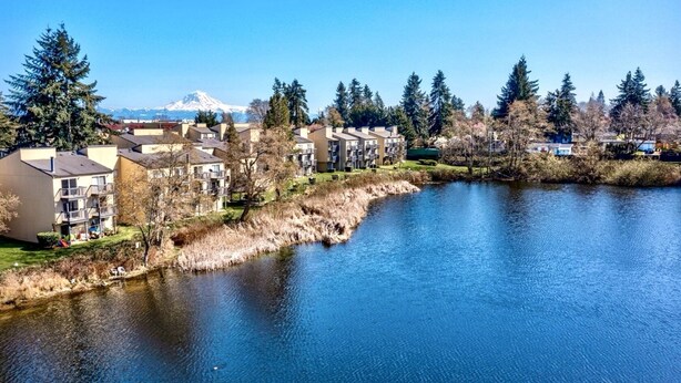 A residential area with apartment buildings along a river, with a mountain in the background.