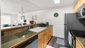 A modern kitchen with a dishwasher, a refrigerator, wooden cabinets, and a granite countertop.
