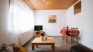 A cozy living room with a wooden ceiling, a TV, a dining table with chairs, and a sofa. - Ferienwohnung Stettner See 42 qm (Rimsting)