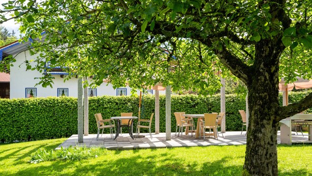An outdoor seating area with tables and chairs, surrounded by a well-maintained lawn and a hedge. - Ferienwohnung Stettner See 42 qm (Rimsting)