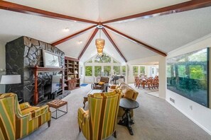 Uma sala de estar espaçosa com lareira, uma janela grande e um espaço de jantar com cadeiras e mesa.