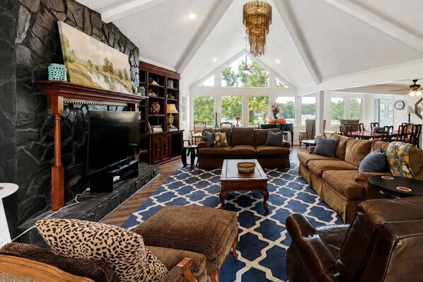 A spacious living room with a fireplace, a television, and a large window overlooking greenery. - Great for Traveling Work Teams /20-30 minutes to downtown Atlanta/Sleeps 12/Private Pool (Jonesboro)