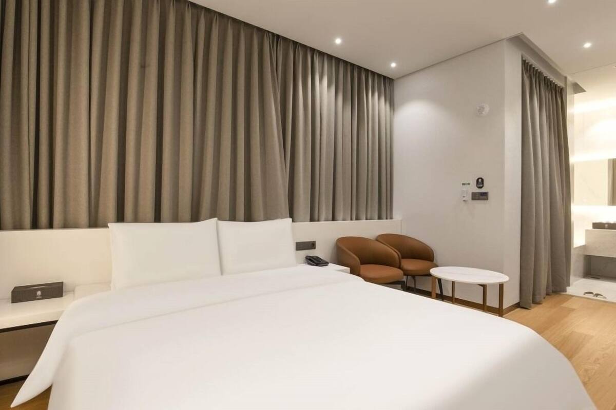 Een moderne hotelkamer met een groot bed, een klein rond tafeltje, een bruine stoel en een bureau met telefoon.