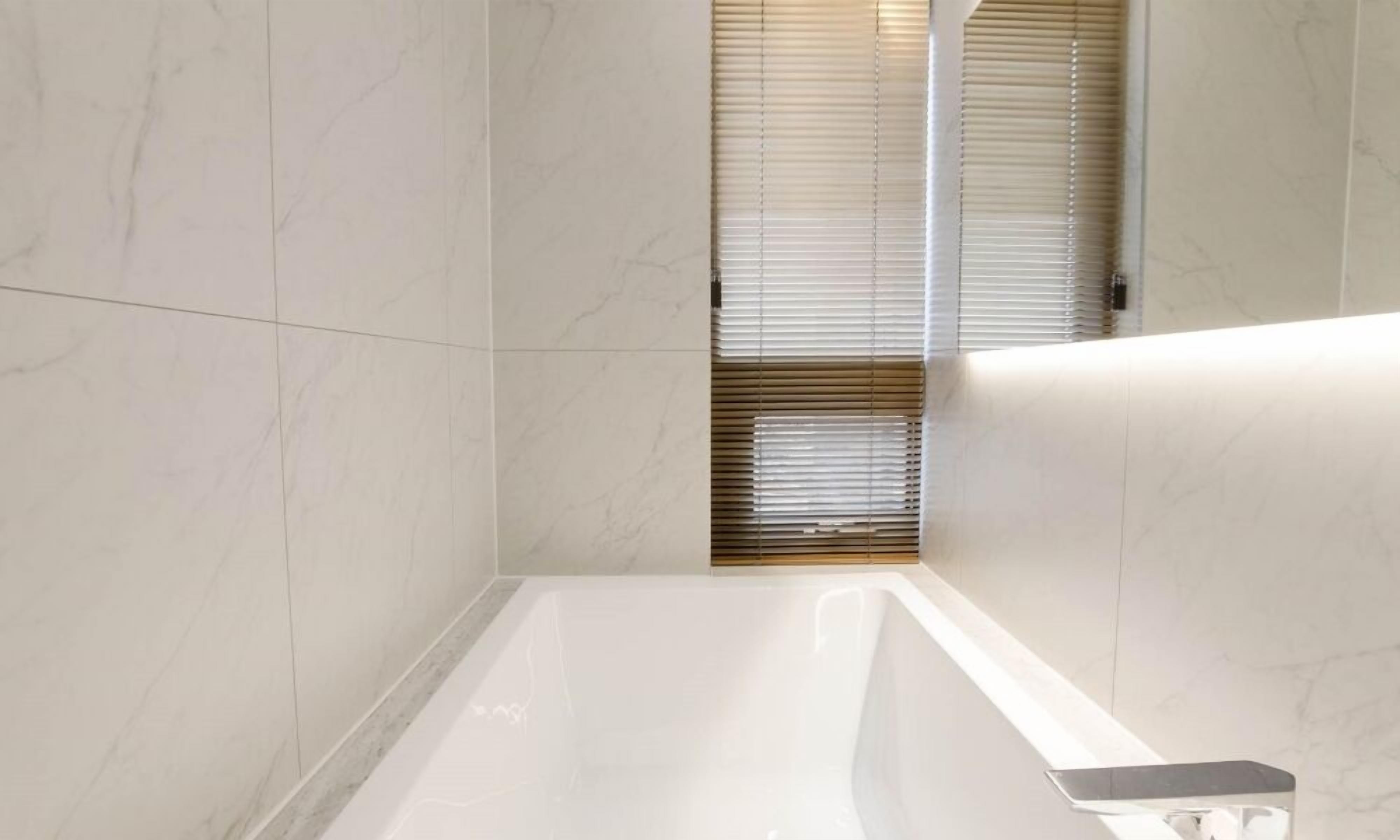 A modern bathroom with a white marble floor, a bathtub, and a wooden window blind.