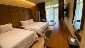 Habitación de hotel con dos camas, un escritorio de madera, una silla, una mesita y un televisor montado en la pared.