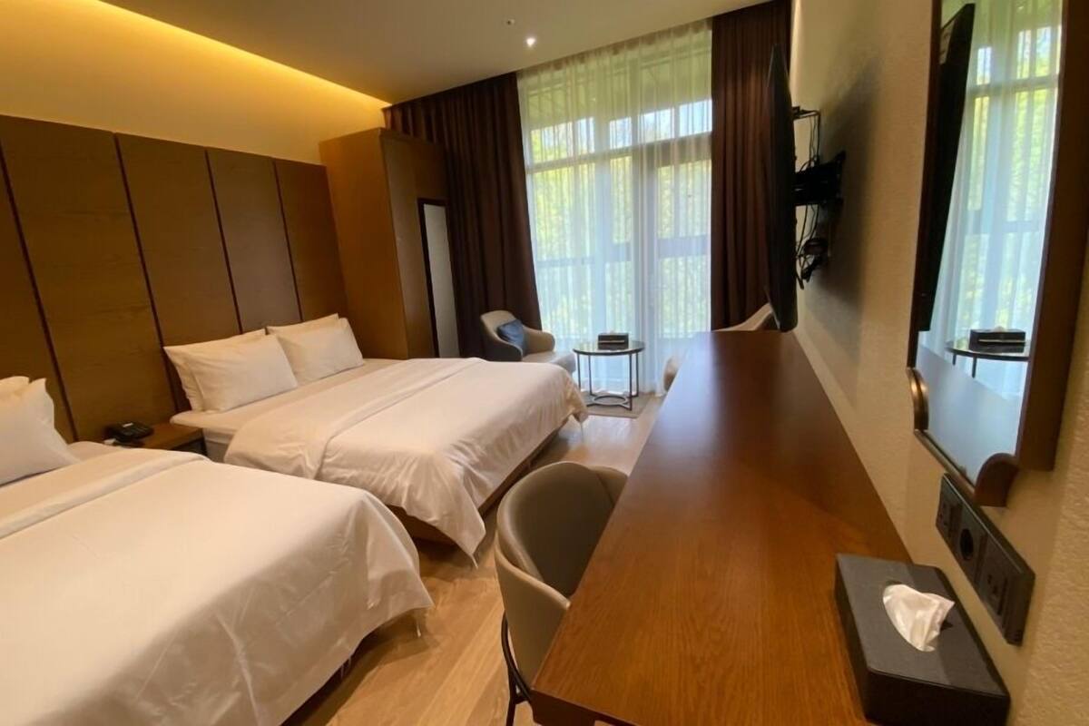 Een hotelkamer met twee bedden, een houten bureau, een stoel, een klein tafeltje en een aan de muur bevestigde televisie.