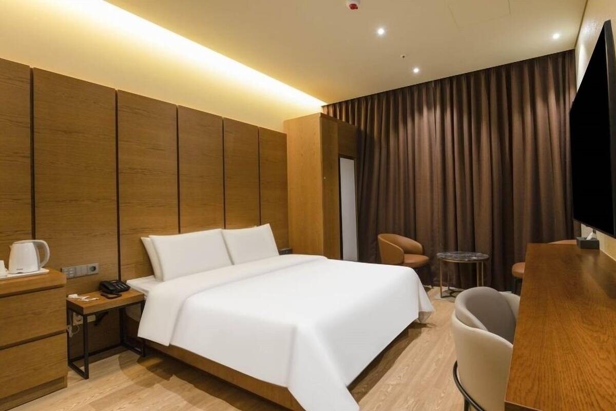 Een moderne hotelkamer met een groot bed, een bureau met telefoon, koffiezetapparaat, televisie en een kleine tafel met twee stoelen.