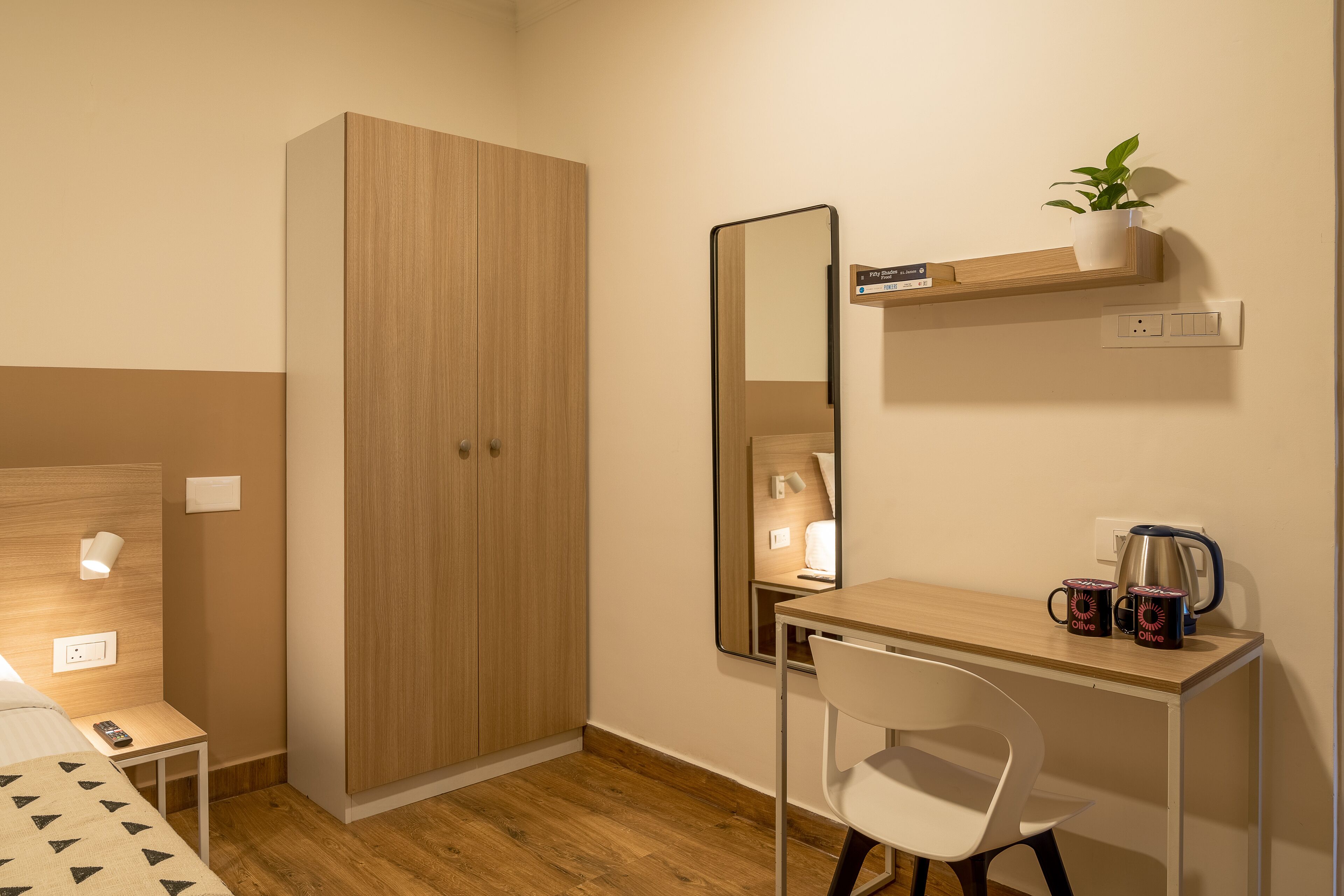 A modern room with a wooden wardrobe, a desk with a chair, a mirror, a shelf with a plant, and a coffee maker.